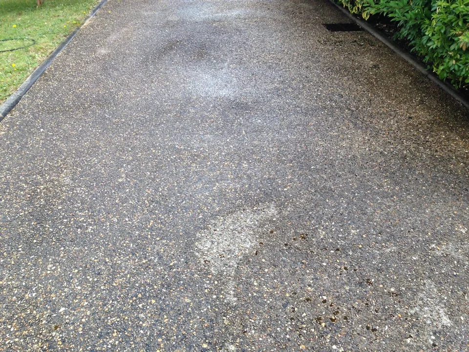 Allée grise bordée de pelouse et de haie, avec grille d’évacuation