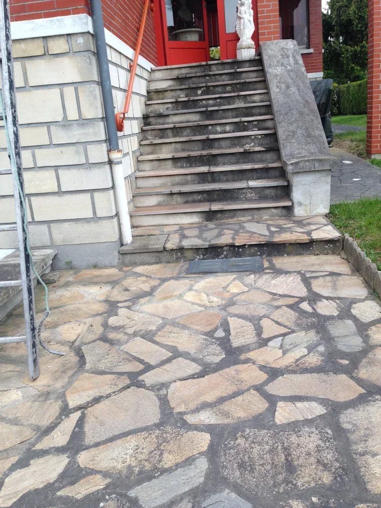 Escalier présentant des traces sombres devant une porte rouge, avec dallage au pied